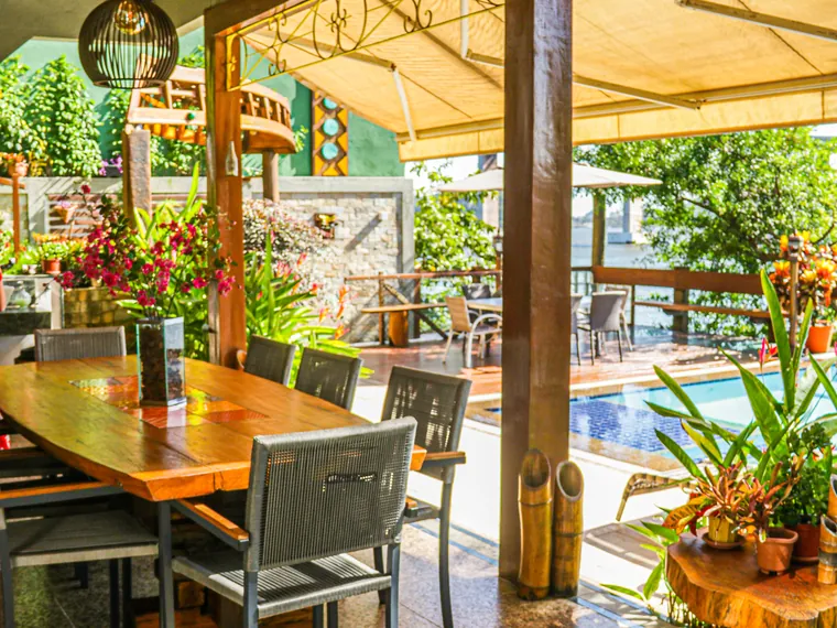 Espaço gourmet coberto com mesa de madeira, cadeiras e a piscina ao fundo