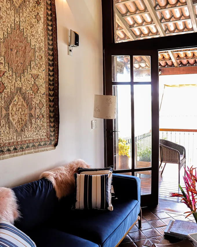 Sala com sofá azul, tapeçaria na parede e porta aberta para a varanda