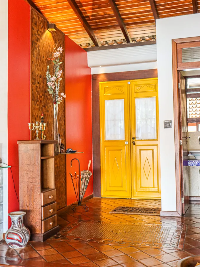 A mesma porta amarela vista de dentro do hall, com parede vermelha e piso de barro