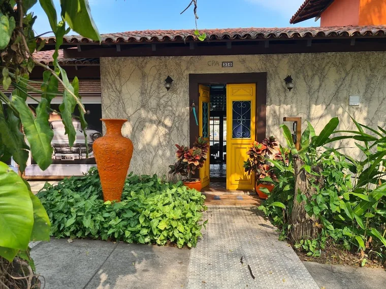 A porta amarela vista da rua, com plantas e um vaso de barro ao lado
